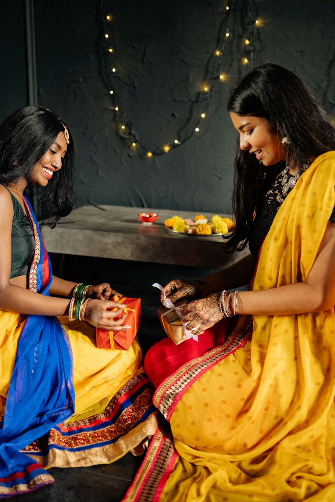 Two women in traditional Indian attire exchanging gifts during a festival.